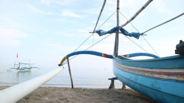 Sahil kıyısında açık gri gökyüzü arka planıyla renkli bir balıkçı teknesi.