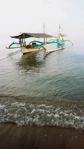 Sahil kıyısında açık gri gökyüzü arka planıyla renkli bir balıkçı teknesi.