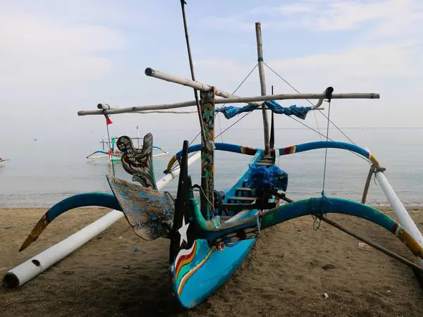 Sahil kıyısında açık gri gökyüzü arka planıyla renkli bir balıkçı teknesi.