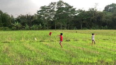 Fabrika bacalarıyla sahada oynayan Endonezyalı çocuklar arka plan olarak duman, kirli hava ve sağlıksız çevre yayıyorlar.