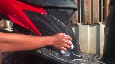 Asyalı Endonezyalı adam motosikletini suyla ve köpüklü süngerle yıkıyor..