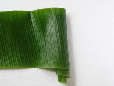 Kıvrık uçlu yeşil muz yaprağı, kopyalama alanı olan beyaz bir zemin üzerinde izole edilmiş, geleneksel Endonezya yemeği veya doğal sanat gibi temalar için uygun.