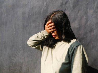 Asyalı üzgün kadın gri arka planda oturuyor. Depresyon, üzüntü, yalnızlık veya zihinsel sağlık konuları için kavramsal görüntü, kopyalama alanı