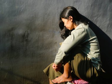 Asyalı üzgün kadın gri arka planda oturuyor. Depresyon, üzüntü, yalnızlık veya zihinsel sağlık konuları için kavramsal görüntü, kopyalama alanı