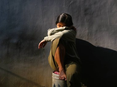 Asyalı üzgün kadın gri arka planda oturuyor. Depresyon, üzüntü, yalnızlık veya zihinsel sağlık konuları için kavramsal görüntü, kopyalama alanı