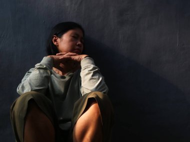 Asyalı üzgün kadın gri arka planda oturuyor. Depresyon, üzüntü, yalnızlık veya zihinsel sağlık konuları için kavramsal görüntü, kopyalama alanı