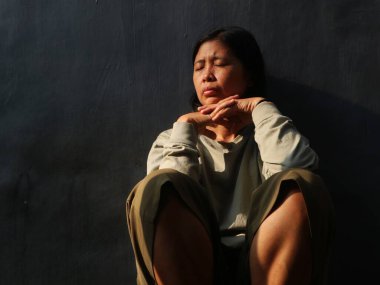 Asyalı üzgün kadın gri arka planda oturuyor. Depresyon, üzüntü, yalnızlık veya zihinsel sağlık konuları için kavramsal görüntü, kopyalama alanı
