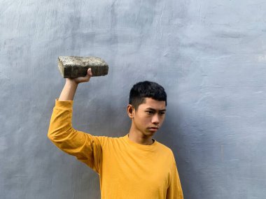 Genç bir adam bir taş bloğuyla saldırmaya hazırlanıyor, tehditkar bir şiddet eylemini ve zorbalık tehdidini yakalıyor.