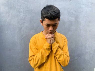 Sarı tişörtlü genç bir adam samimi bir duayla ve sessiz bir yansımayla yakalanır. Hristiyan ve ilham verici bir İncil dizesi geçmişi için mükemmeldir.