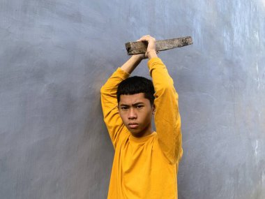 Genç bir çocuk bir tahta blokla saldırmaya hazırlanıyor, tehditkar bir şiddet eylemini ve zorbalık tehdidini yakalıyor.