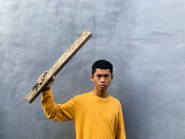 Genç bir çocuk bir tahta blokla saldırmaya hazırlanıyor, tehditkar bir şiddet eylemini ve zorbalık tehdidini yakalıyor.