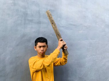 Genç bir çocuk bir tahta blokla saldırmaya hazırlanıyor, tehditkar bir şiddet eylemini ve zorbalık tehdidini yakalıyor.