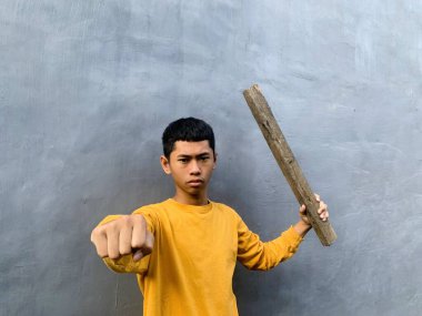 Genç bir çocuk bir tahta blokla saldırmaya hazırlanıyor, tehditkar bir şiddet eylemini ve zorbalık tehdidini yakalıyor.