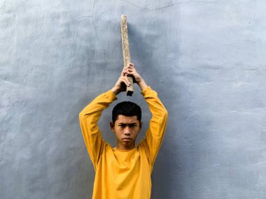 Genç bir çocuk bir tahta blokla saldırmaya hazırlanıyor, tehditkar bir şiddet eylemini ve zorbalık tehdidini yakalıyor.