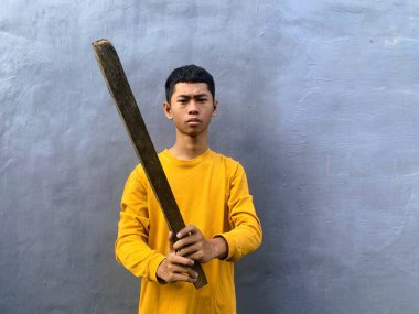 Genç bir çocuk bir tahta blokla saldırmaya hazırlanıyor, tehditkar bir şiddet eylemini ve zorbalık tehdidini yakalıyor.