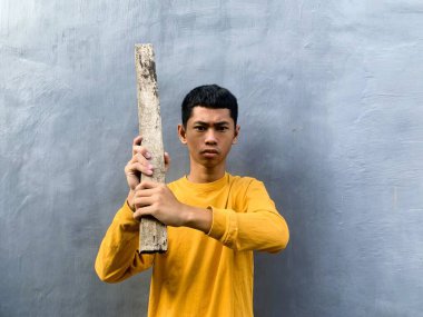 Genç bir çocuk bir tahta blokla saldırmaya hazırlanıyor, tehditkar bir şiddet eylemini ve zorbalık tehdidini yakalıyor.