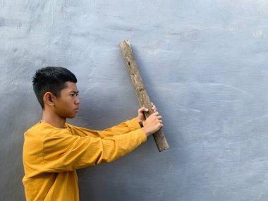 Genç bir çocuk bir tahta blokla saldırmaya hazırlanıyor, tehditkar bir şiddet eylemini ve zorbalık tehdidini yakalıyor.