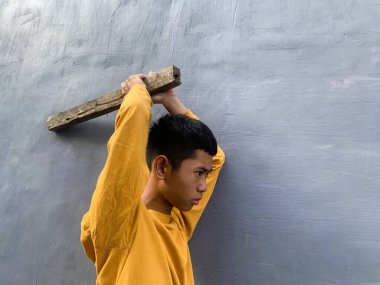 Genç bir çocuk bir tahta blokla saldırmaya hazırlanıyor, tehditkar bir şiddet eylemini ve zorbalık tehdidini yakalıyor.