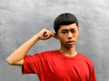 A surprised, startled, and funny southeast asian teenager pulls their own ear with an expressive face