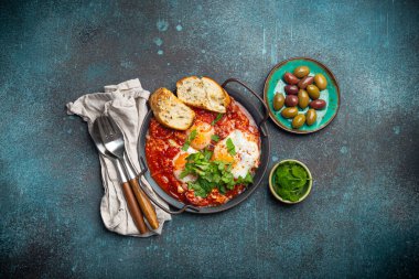 Orta Doğu ve Maghrebi 'nin sağlıklı yemekleri Shakshouka yumurtalar ve domates sosu tavada servis edilir tostlar, taze kişniş ve yukarıdaki kırsal beton arka plan masasında zeytinler.