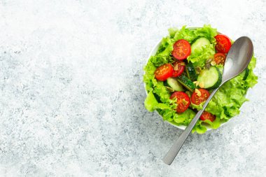 Taze salatalıklı sağlıklı sebze salatası, domates, taze buzdağı salatası kabı içinde bir kaşık ile kırsal beyaz beton masa manzarası. Diyet konsepti için sebze salatası, metin için boşluk