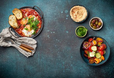 Orta Doğu geleneksel kahvaltısı ya da Shakshouka yumurtalı brunch tostlar, taze sebze salatası, humus ve zeytinler yukarıdan gelen kırsal beton arka plan masasında, metin için boşluk