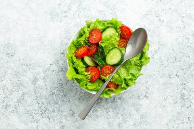 Taze salatalıklı sağlıklı sebze salatası, domates, taze buzdağı salatası kabı içinde bir kaşık ile kırsal beyaz beton masa manzarası. Diyet ve sağlıklı beslenme için sebze salatası.