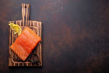 Ahşap mutfak kesme tahtasındaki taze çiğ somon filetosu baharat ve koyu kahverengi kırsal arka planda limon üst görünümü, metin için boşluk