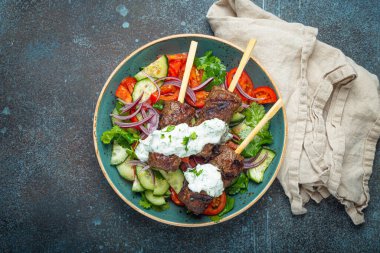 Grilled skewer meat beef kebabs on sticks served with fresh vegetables salad on plate on rustic concrete background from above. Traditional Middle Eastern and Turkish dish Kebab, space for text
