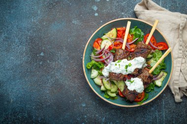Grilled skewer meat beef kebabs on sticks served with fresh vegetables salad on plate on rustic concrete background from above. Traditional Middle Eastern and Turkish dish Kebab, space for text