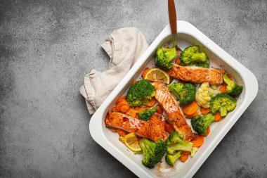 Top view of healthy baked fish salmon steaks, broccoli, cauliflower, carrot in casserole dish on gray stone background. Cooking a delicious low carb dinner, healthy nutrition concept. Space for text