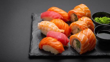 Set of traditional Japanese sushi and rolls angle view with soy sauce and wasabi on dark black rustic slate. Sushi with salmon, tuna and shrimp