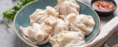 Georgian dumplings Khinkali on plate with red tomato sauce and fresh cilantro angle view on rustic stone background, traditional dish of Georgia