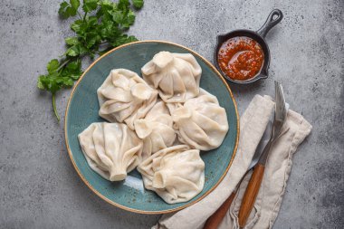 Georgian dumplings Khinkali on plate with red tomato sauce and fresh cilantro top view on rustic stone background, traditional dish of Georgia