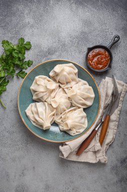 Georgian dumplings Khinkali on plate with red tomato sauce and fresh cilantro top view on rustic stone background, traditional dish of Georgia