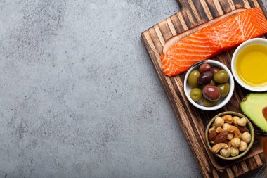 Food sources of healthy unsaturated fat and omega 3: fresh raw salmon fillet, avocado, olives, nuts on cutting board, rustic stone background top view. Healthy nutrition and keto diet, space for text