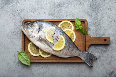 Çiğ çiğ balık dorado, limon ve taze fesleğen ile ahşap kesme tahtası, kırsal taştan arka planda bıçakla üst manzara, sağlıklı balık dorado kavramı.