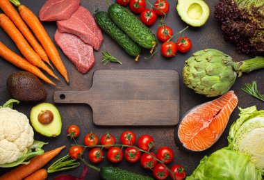 Çeşitli gıda ham ürünleri: sebzeler, sığır eti, balık somonu ve ortada boş tahta kesme tahtası, koyu kırsal kahverengi masa üstü manzarası. Sağlıklı beslenme geçmişi, dengeli beslenme malzemeleri