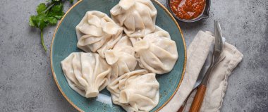Georgian dumplings Khinkali on plate with red tomato sauce and fresh cilantro top view on rustic stone background, traditional dish of Georgia