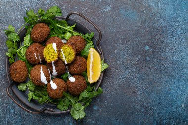 Plate of fried falafel balls served with fresh green cilantro and lemon top view on rustic concrete background. Traditional vegan dish of Middle Eastern cuisine, space for text