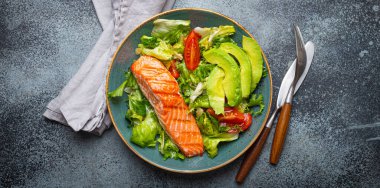 Izgara balık somon bifteği ve sebze salatası. Avokado ile birlikte, seramik tabakta, taşralı arka plan görüşü, dengeli diyet veya somon ve sebzelerle sağlıklı beslenme salatası yemeği.