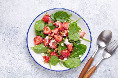 Taze çilekli hafif sağlıklı yaz salatası, ıspanak, krem peynir ve ceviz beyaz seramik tabakta, beyaz kırsal taş arka plan üst görünümü.