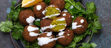 Yeşil kişniş ve limonla servis edilen kızarmış falafel köftesi tabağı kırsal beton arka planda. Geleneksel Orta Doğu mutfağı vegan yemeği.