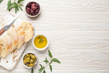 Mutfak tahtasında dilimlenmiş taze ciabatta, yeşil ve kahverengi zeytin, biberiyeli zeytin yağı, zeytin ağacı dalları, beyaz ahşap rustik arka plan üst görünüm boşluğu