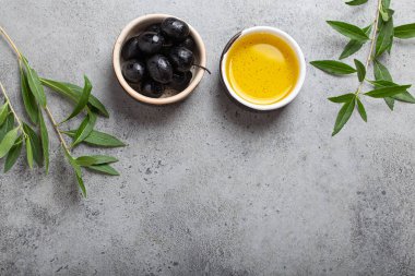 Siyah zeytin ve ekstra saf zeytin yağı küçük bir kasede zeytin dalları gri beton arka planda üst görünüm, metin için boşluk