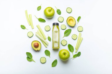 Yeşil meyve ve sebzelerle çevrili bir şişe yeşil smoothie: elma, avokado, ıspanak, kereviz çubukları, beyaz arka planda salatalık. Diyet, sağlıklı beslenme, detoks konsepti