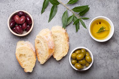 Taze ciabatta dilimleri, yeşil ve kahverengi zeytin, biberiyeli zeytin yağı, üzerinde gri beton taştan kırsal arka planda zeytin ağacı dalları