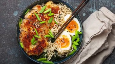 Asya erişteli ramen çorbası, bol yağda kızartılmış panko tavuklu fileto ve haşlanmış yumurta, pirzola çubukları ve soya sosu ile birlikte taş kırsal masada yavaşça dönüyor. Yüksek kalite 4k görüntü