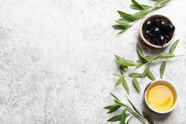 Siyah zeytinyağı ve ekstra saf zeytin yağı küçük bir kâse içinde zeytin dalları beyaz beton arka planda üst görünüm, boşluk kopyala