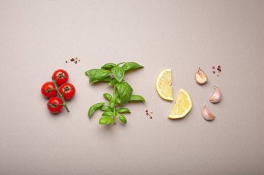 Sağlıklı besin maddelerine sahip kompozisyon: taze kiraz domatesleri, fesleğen dalı, sarımsak karanfilleri, minimalist gri arkaplan üzerindeki limon kamaları, tepeden çekim